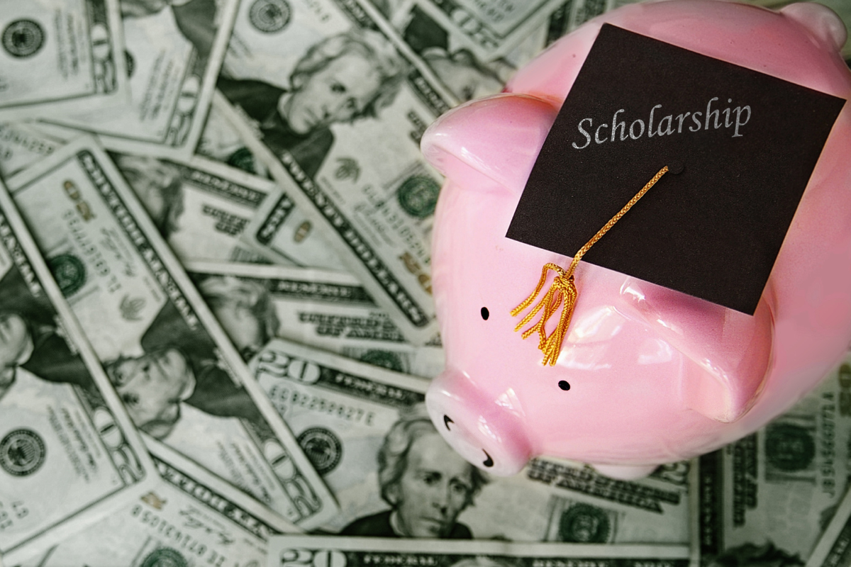 Piggy bank wearing graduation cap with "scholarship" on it standing on money