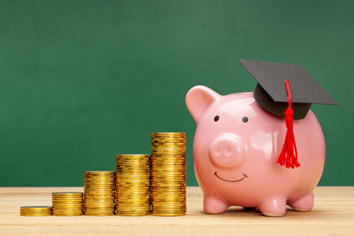 Smiling piggy bank wearing graduation cap next to steadily growing piles of coins
