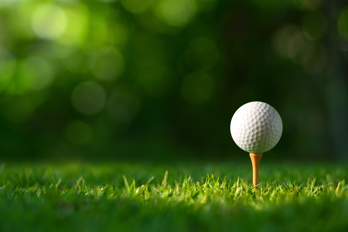 Close-up golf ball on tee with blur green bokeh background