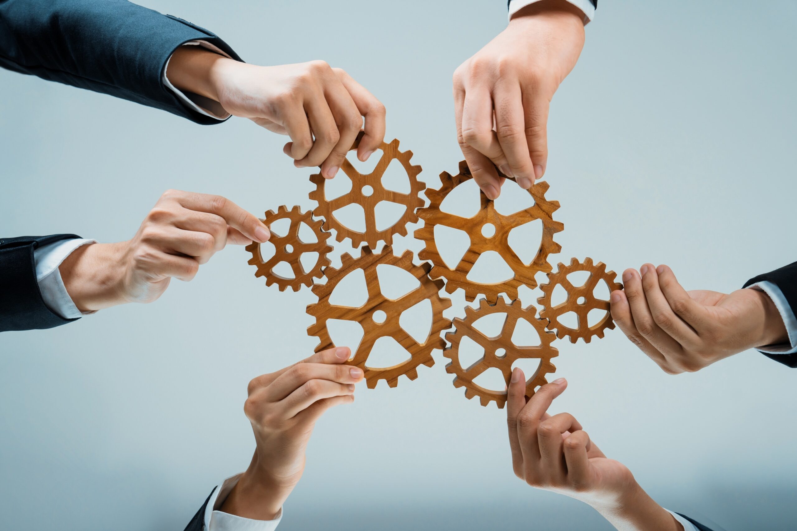 Multiple hands holding cogwheels close together