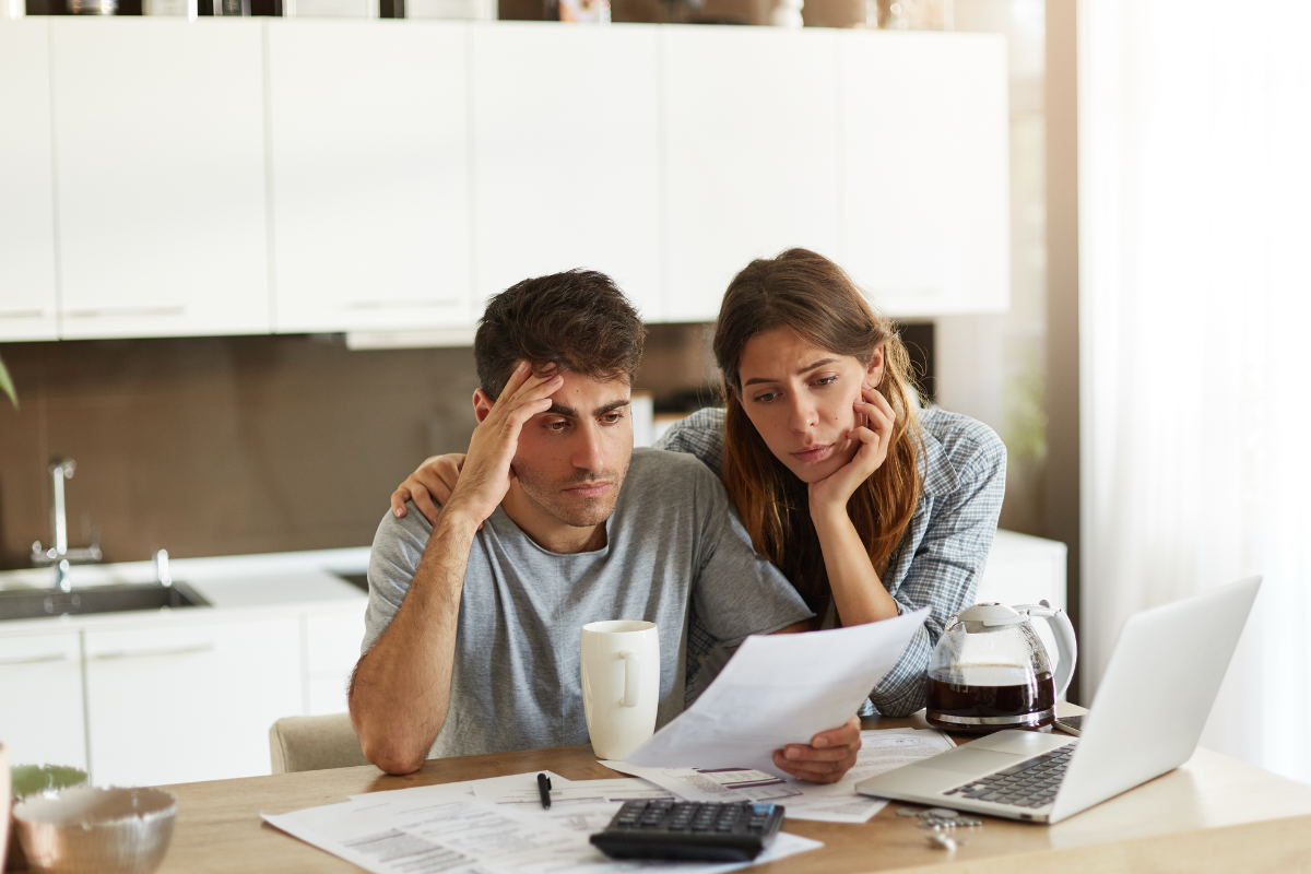 Unhappy American couple managing home accounts in kitchen, trying to save some money by cutting family expenses. Finances, bankruptcy, taxes, money, accounting and financial problems concept