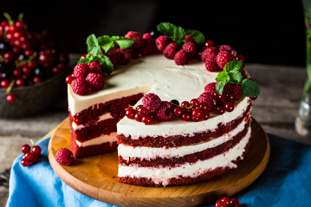 Red velvet cake decorated with berries with slice taken out of it