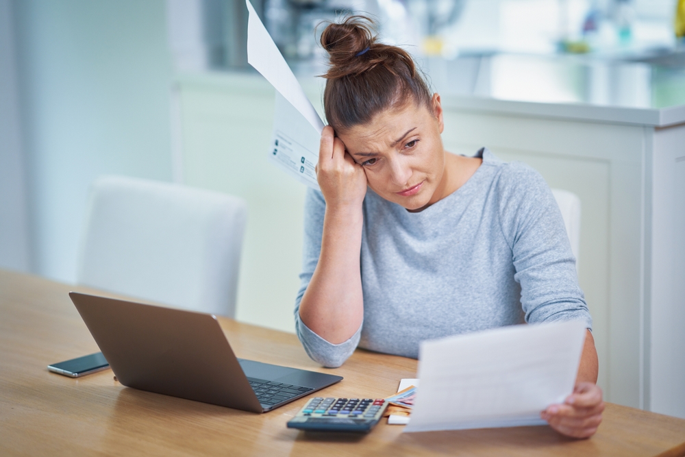 Worried woman looking at financial papers, laptop on table