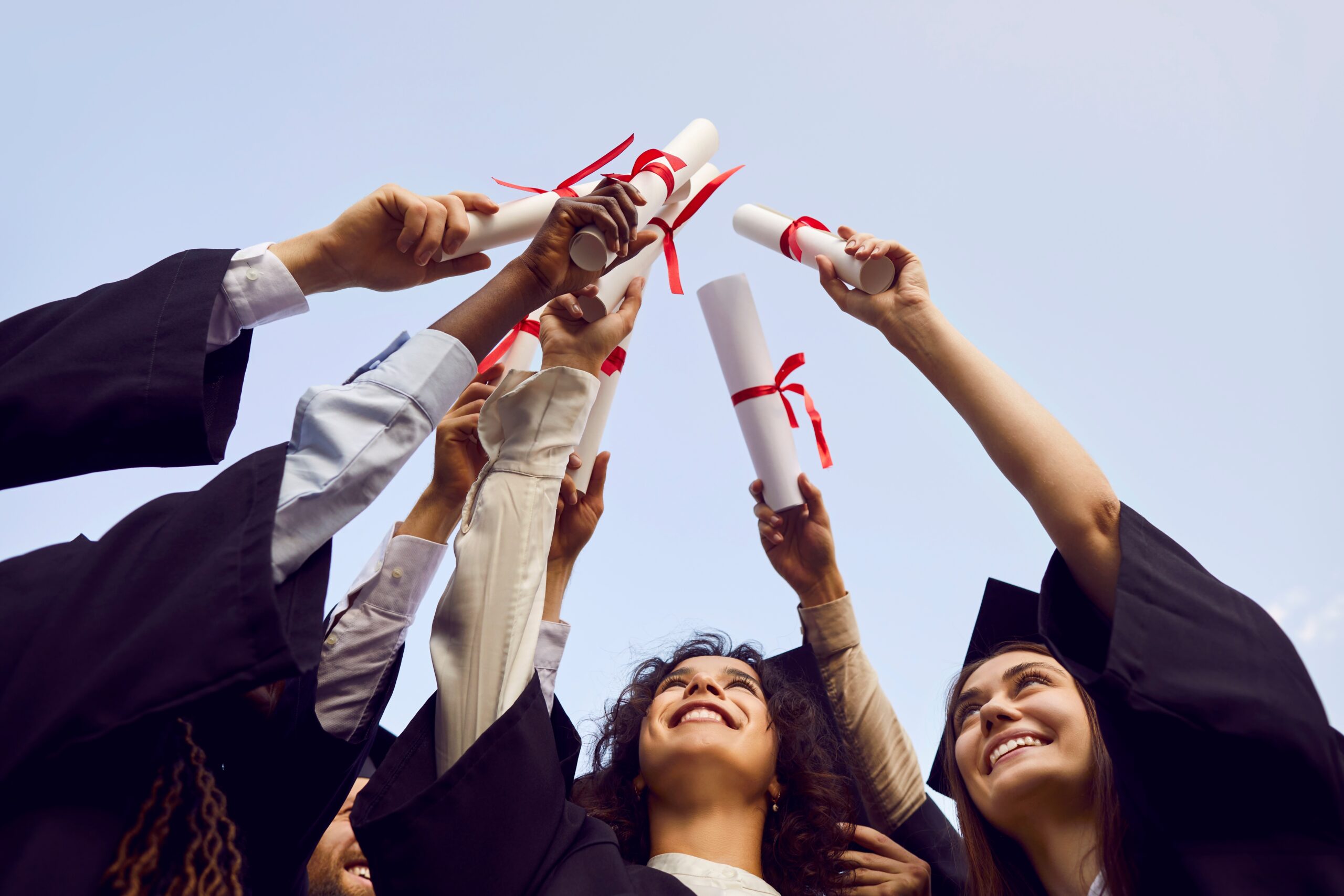 Happy college students holding up diplomas