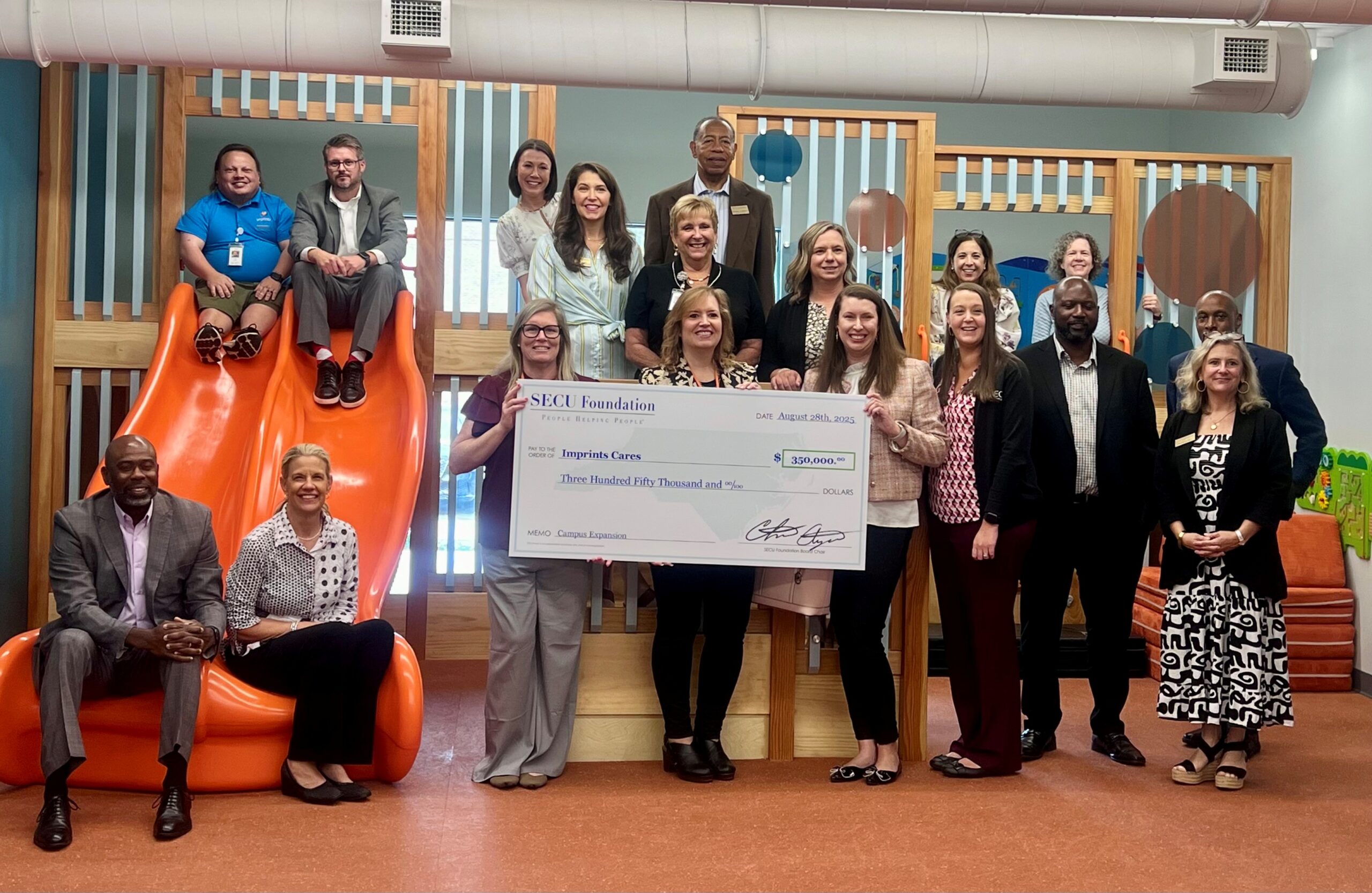 Holding the check left to right are IC Director of Development and External Relations Carrie Pasquale, IC Interim Executive Director Kim Turner-Kendricks, and SECU Lexington Branch Vice President Laura Goins surrounded by IC, SECU, and SECU Foundation representatives.