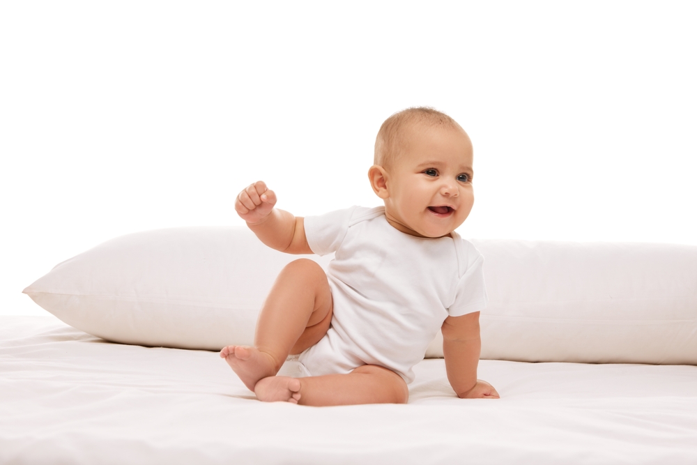 Smiling baby sitting on top of bed