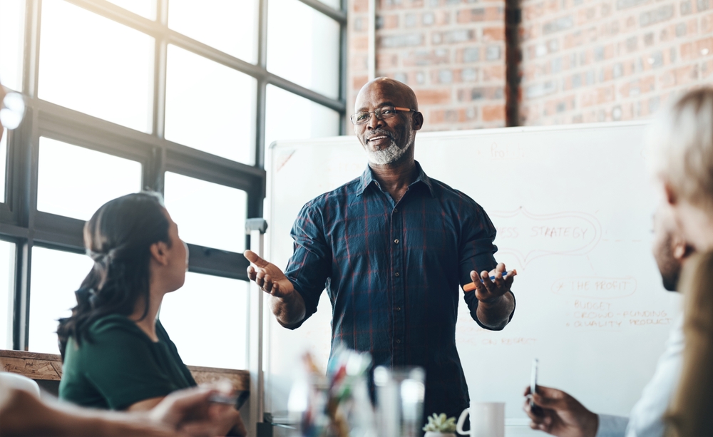 Man presenting in front of colleagues while standing in front of whiteboard