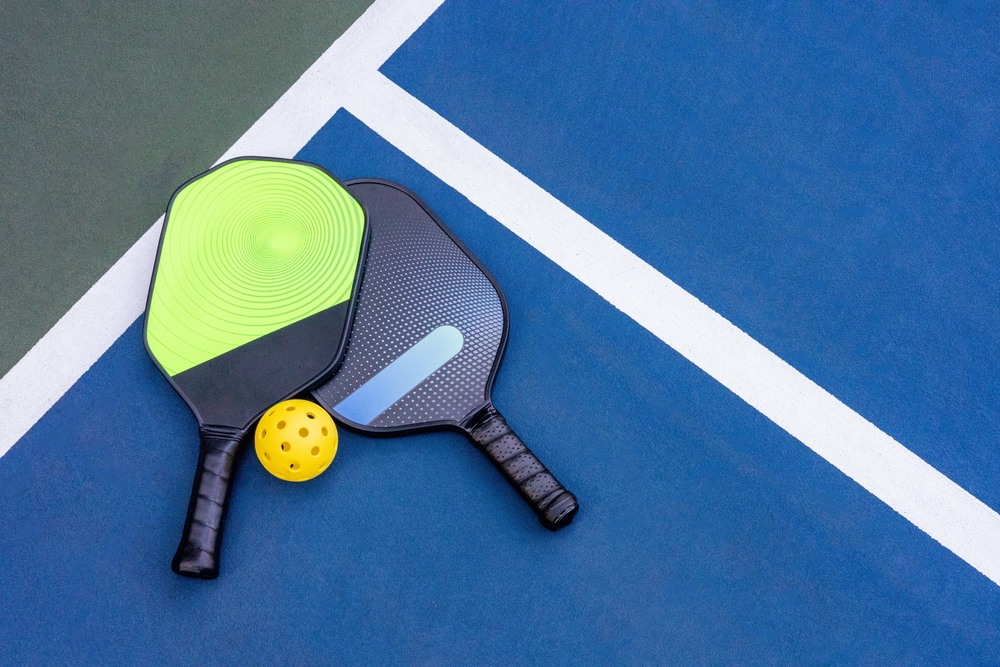 Two pickleball racquets and ball on the ground of court