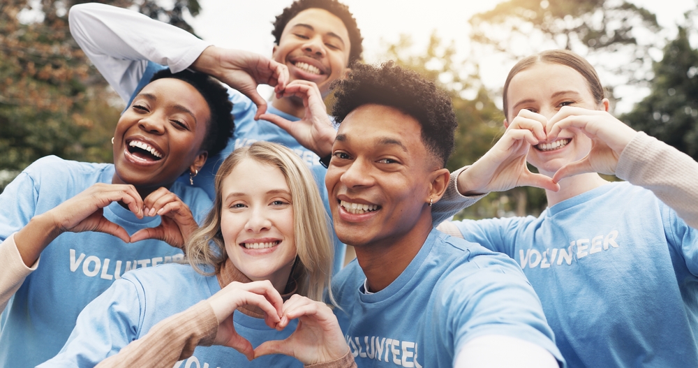 Group of volunteers smiling and forming shape of heart with hands