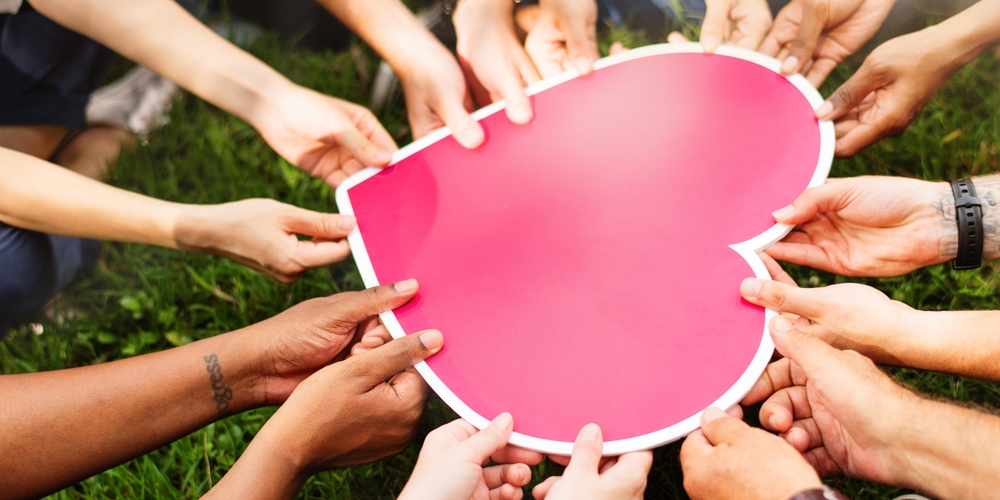Multiple hands holding a large pink heart