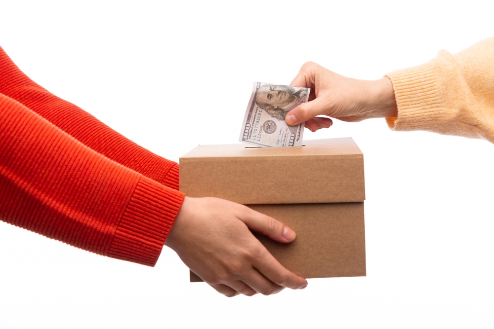 Person holding cardboard box; another person putting $100 bill into cardboard box