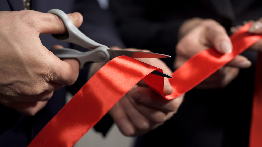 Hands holding scissors cutting red ribbon