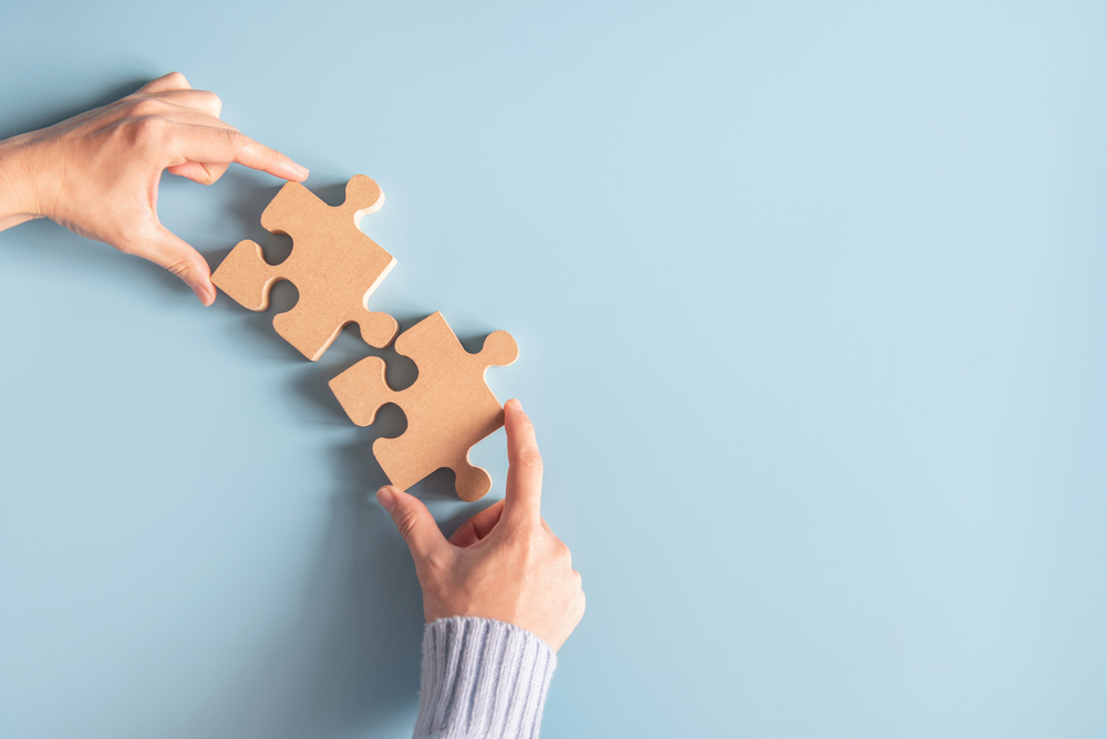 Hands bringing two wooden puzzle pieces together