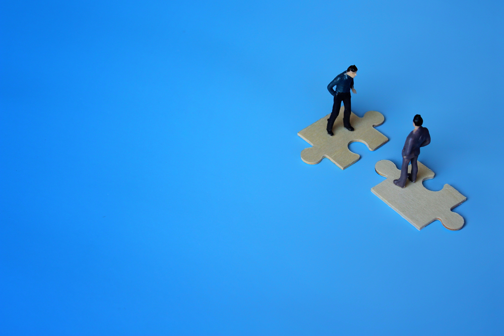 Figures of two businessmen on top of two puzzle pieces