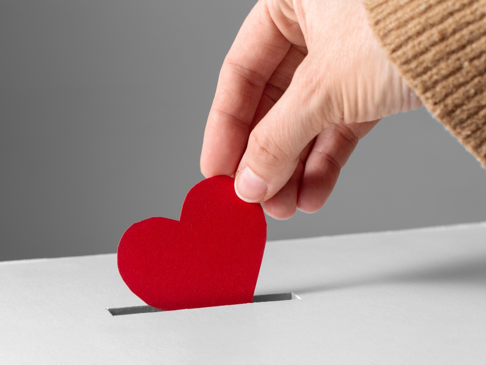 Person putting red heart into slot of donation box