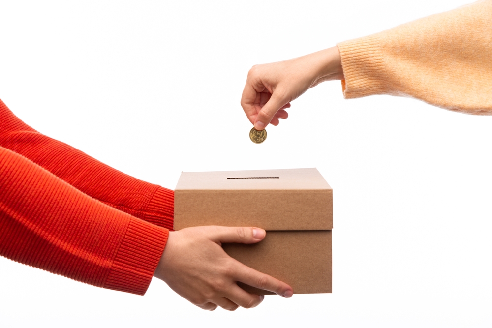 Person holding cardboard donation box; person putting coin into donation box