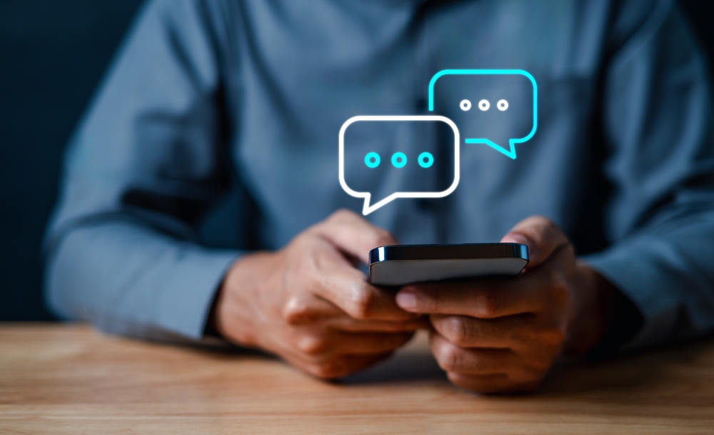 Man holding smartphone; text bubbles with three dots in them above smartphone
