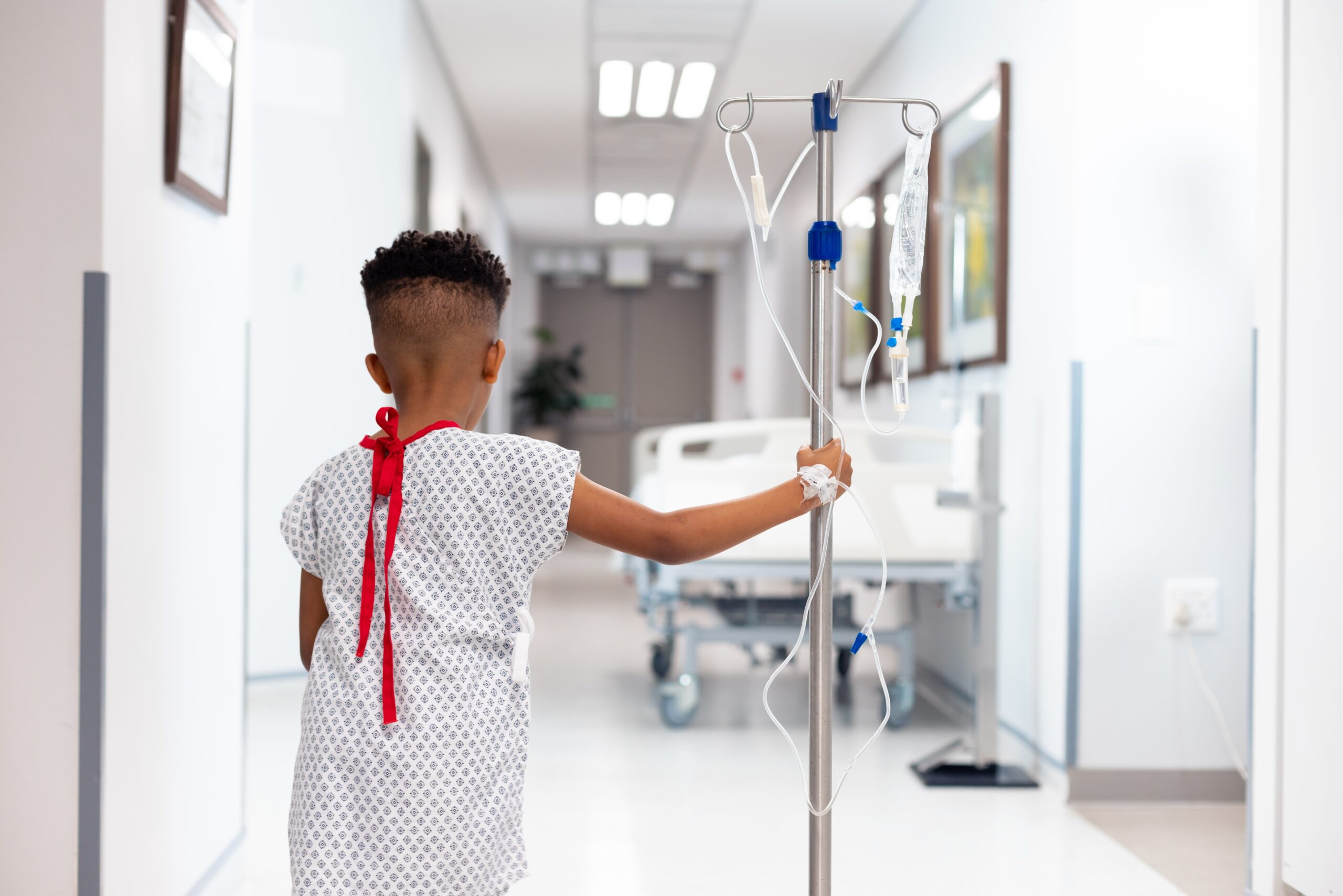 Rear view of african american boy patient walking with drip stand in hospital with copy space. Hospital, medical and healthcare services.