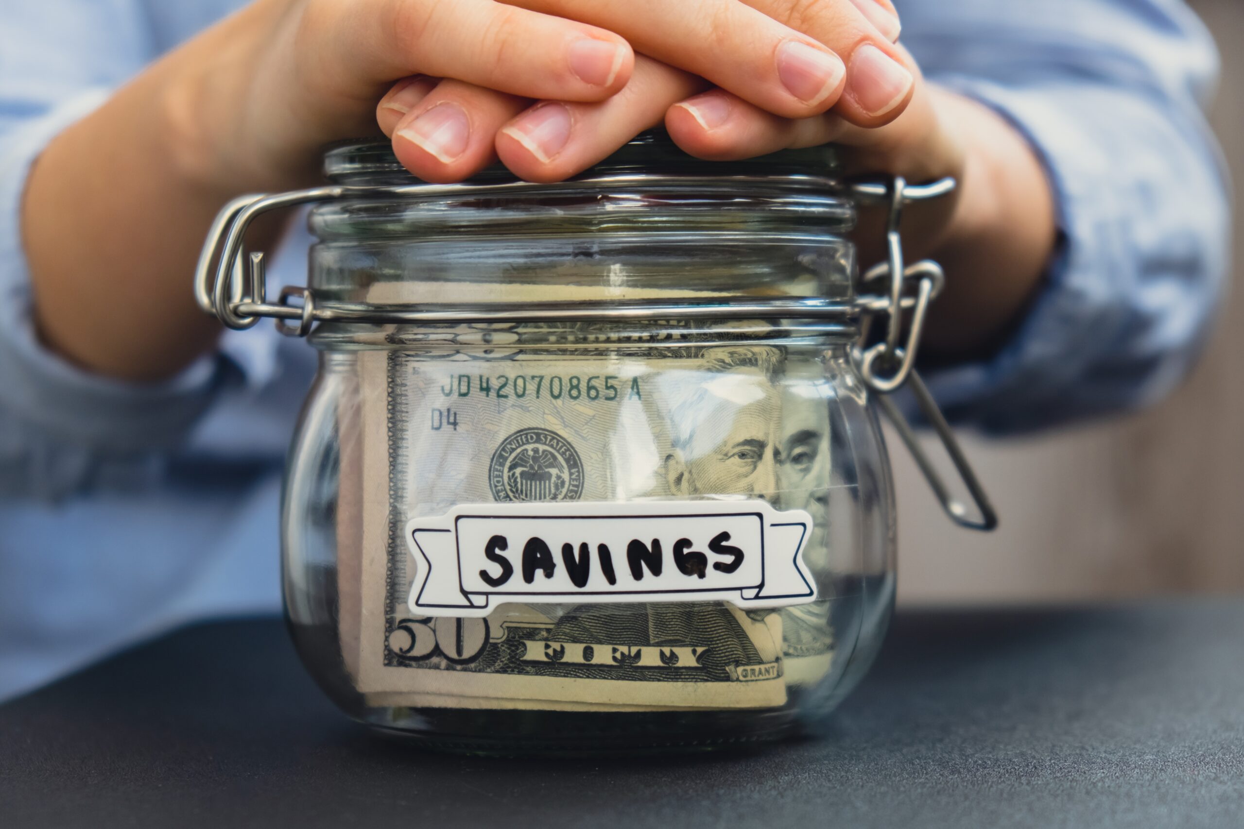 Unrecognizable woman holding Saving Money In Glass Jar filled with Dollars banknotes. SAVINGS transcription in front of jar. Managing personal finances extra income for future insecurity