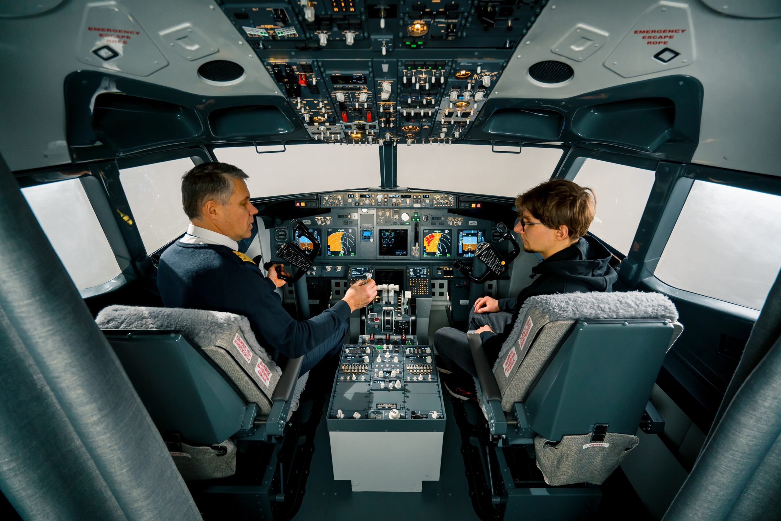 An experienced pilot instructs a young student before a training flight in the cockpit of aero simulator