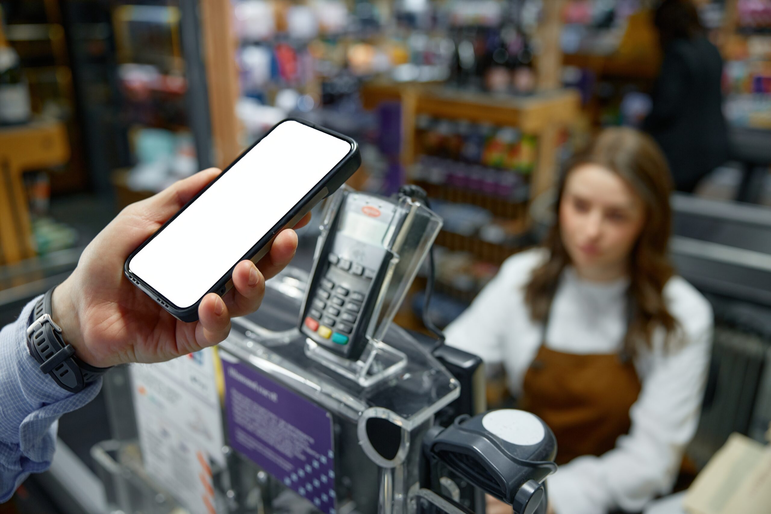 An individual is holding a mobile cell phone in front of a cash register