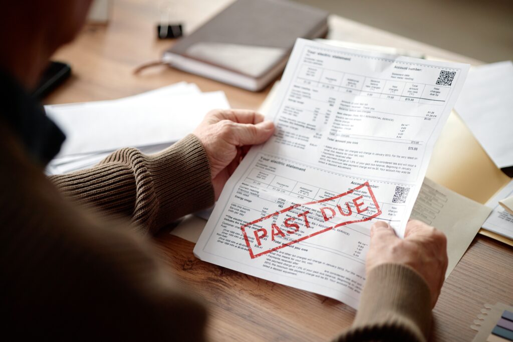Adult man holding past due invoice, analyzing financial documents at desk, hands reviewing overdue bill paperwork, focusing on payment and expense management