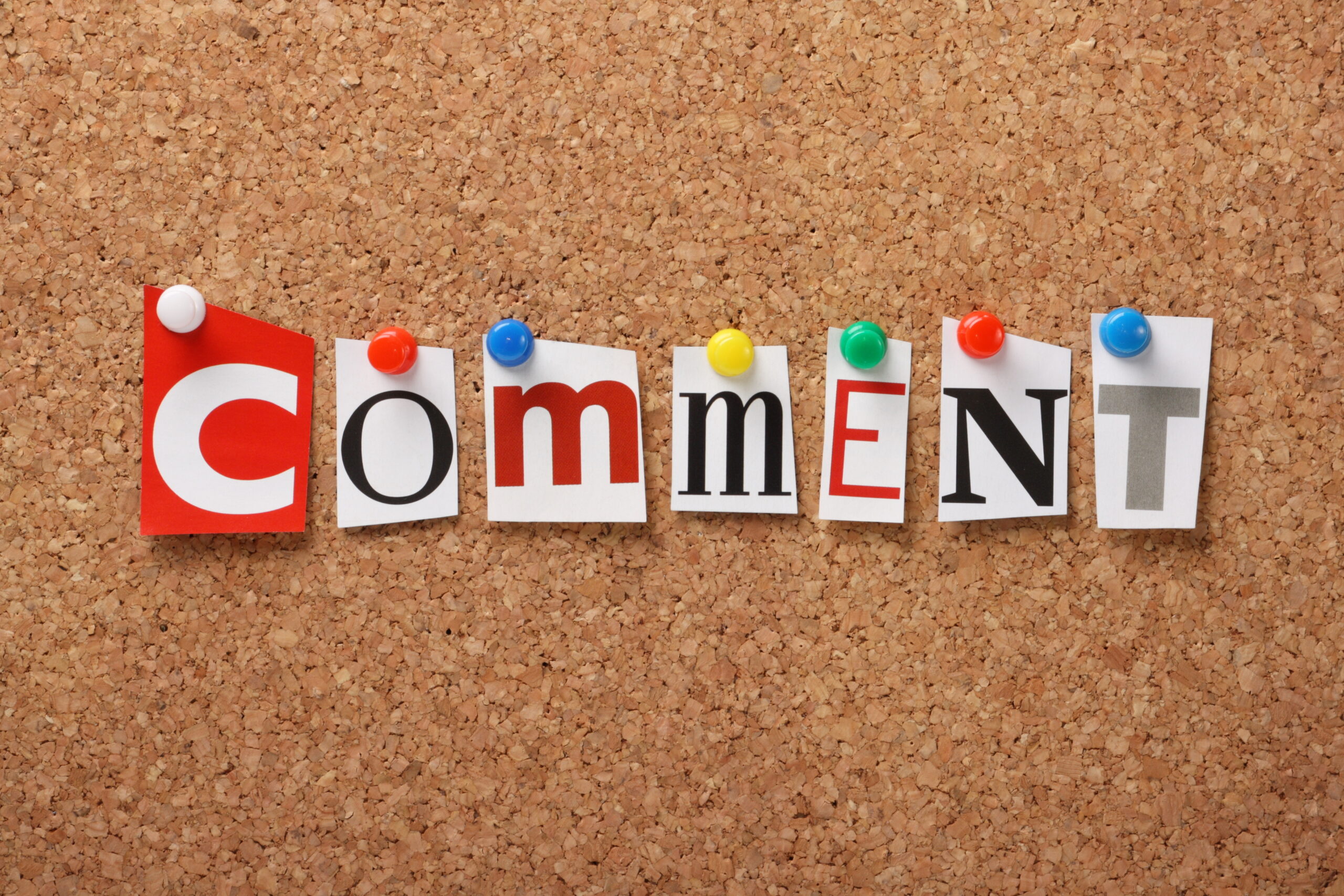 The word Comment in cut out magazine letters pinned to a cork notice board.