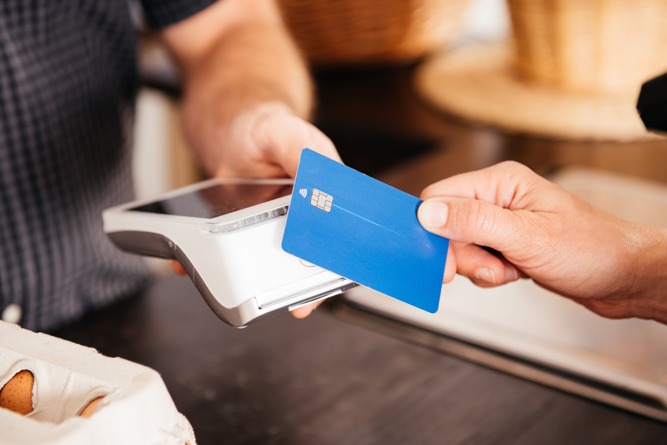 A customer is paying for groceries using a credit card, swiping it through a card reader at the stores checkout counter.