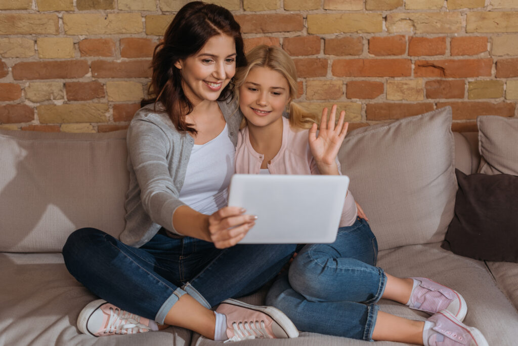 Selective focus of smiling kid and mother having video call on digital tablet on couch