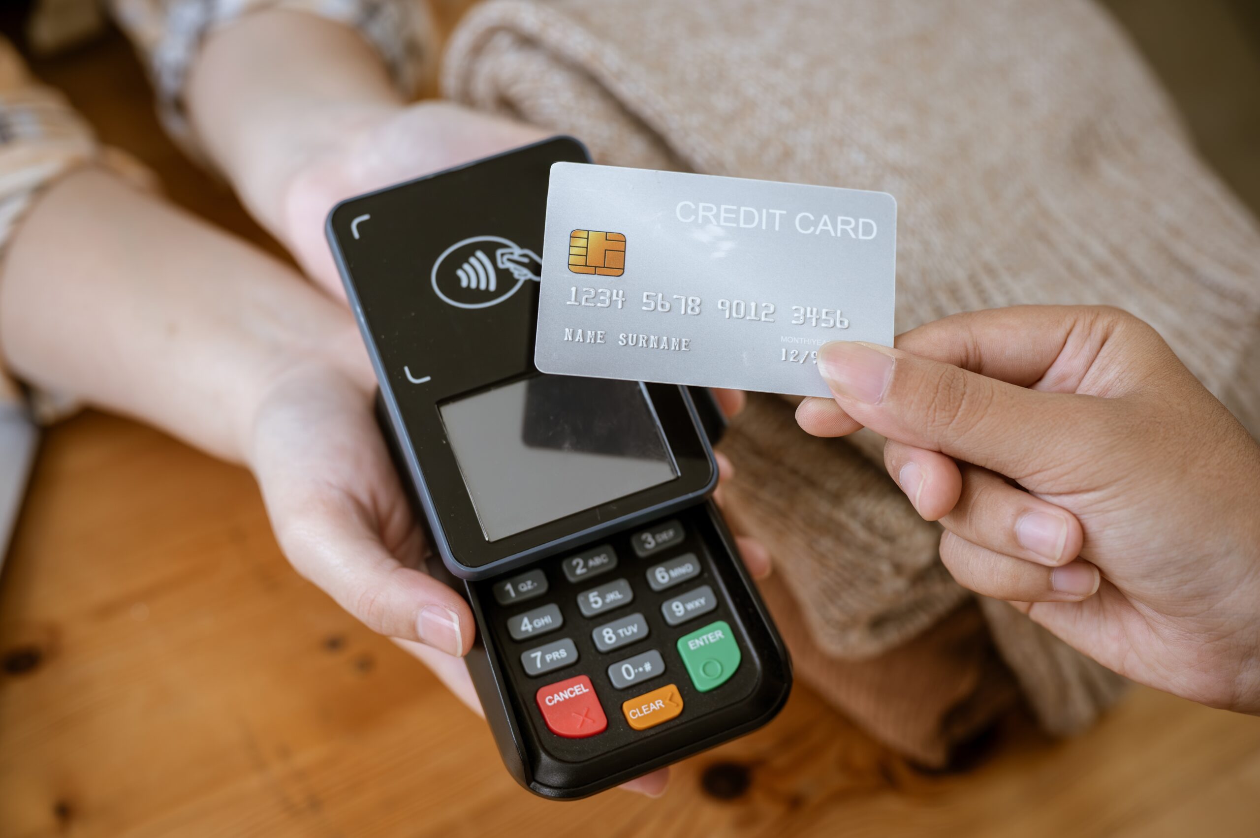 A close-up image of a customer tapping her credit card with a payment terminal or credit card machine at a cashier in a clothing store. cashless payment, card reader, electronic funds transfer