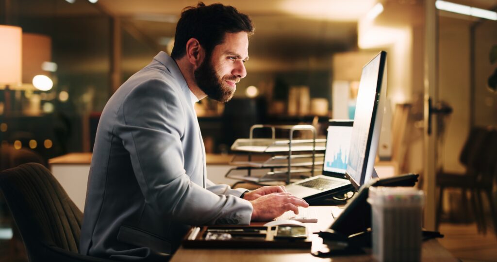 Business, night and man in office, computer and internet for stats, financial agency and stock market. Evening, person and employee in workplace, pc and online reading for economy info and trading