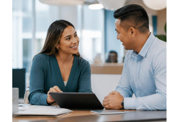A friendly credit union employee having an open, reassuring conversation with a customer across a desk.