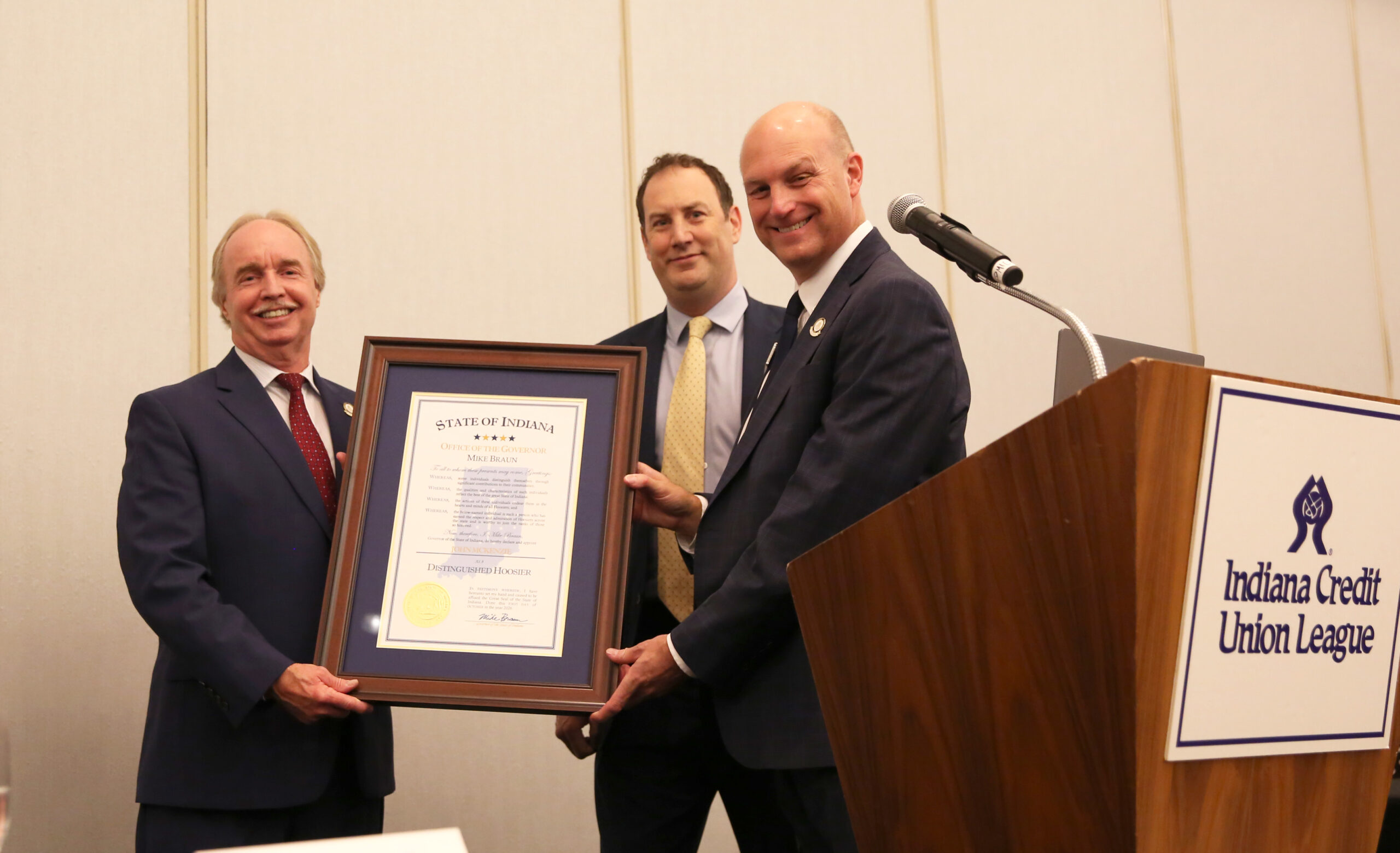 2. Distinguished Hoosier – McKenzie and League President Chris Beaumont hold the award, which was presented on behalf of Gov. Mike Braun by Chris Dietz of the Indiana Department of Financial Institutions (yellow tie).